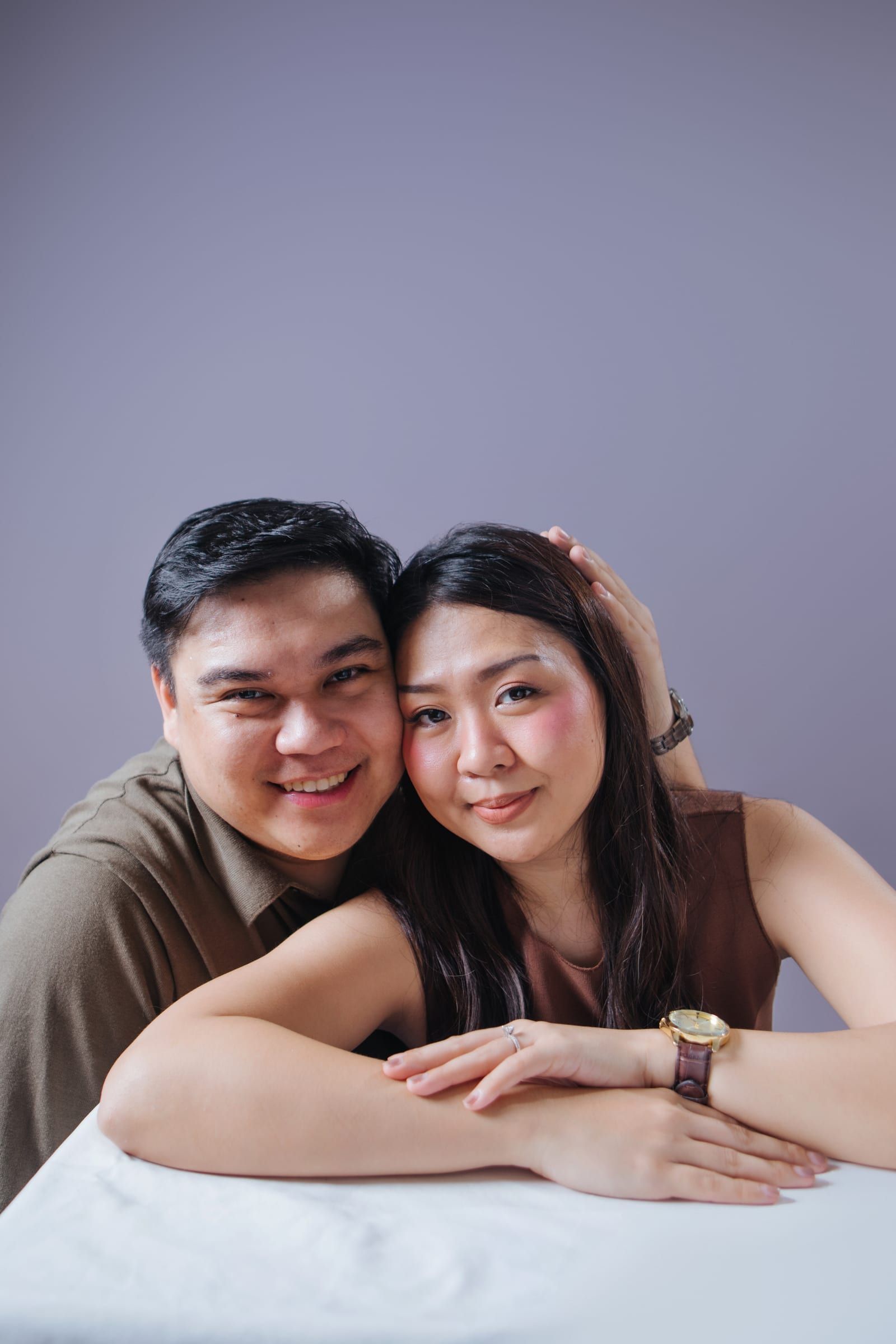 Now: Joboy and Anna sit cheek to cheek at a white table, smiling at the camera, his hand resting on her head and her arms folded in front.