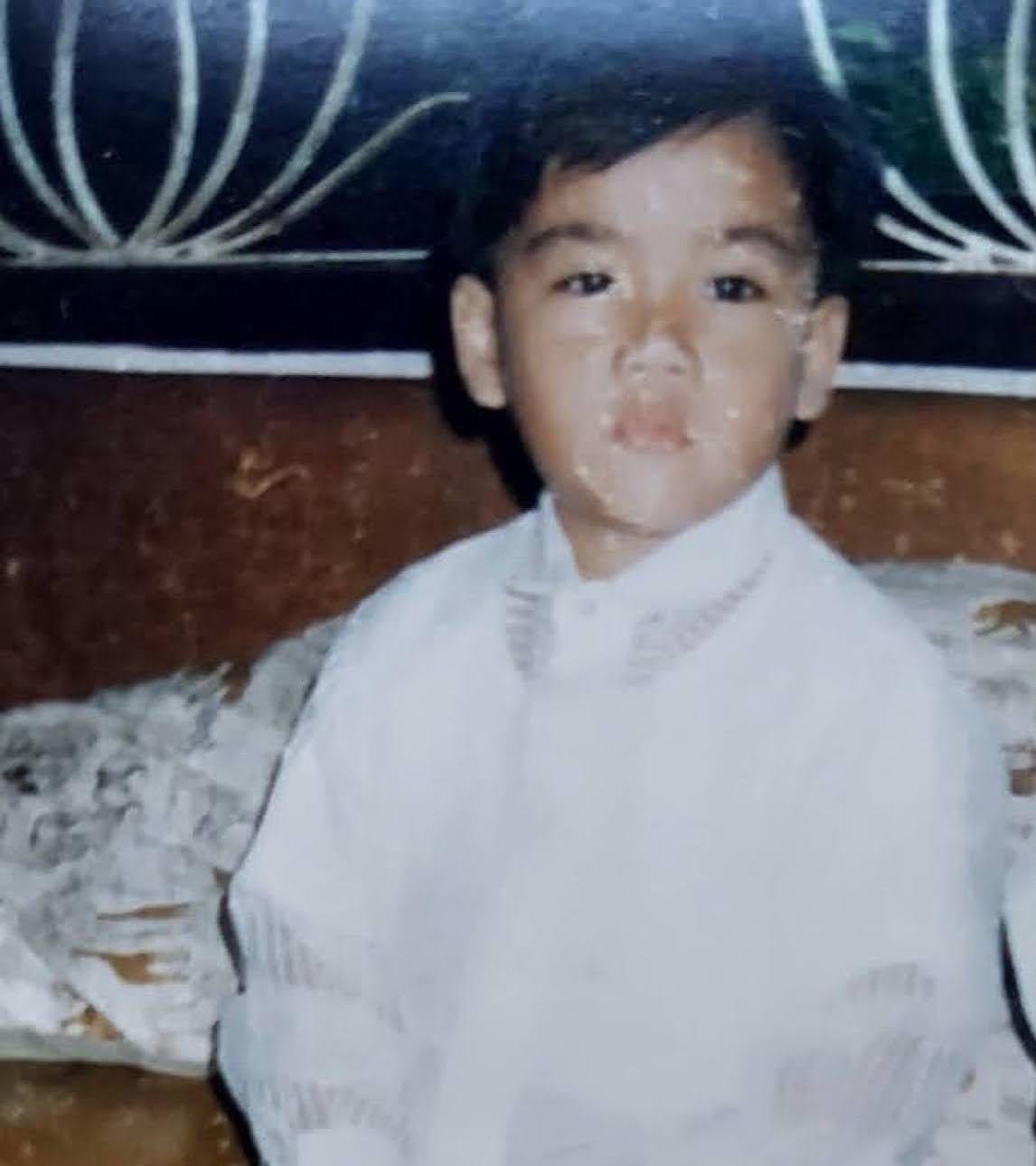 Then: Joboy as a little boy in a white barong-style shirt, sitting in front of a wrought-iron window.